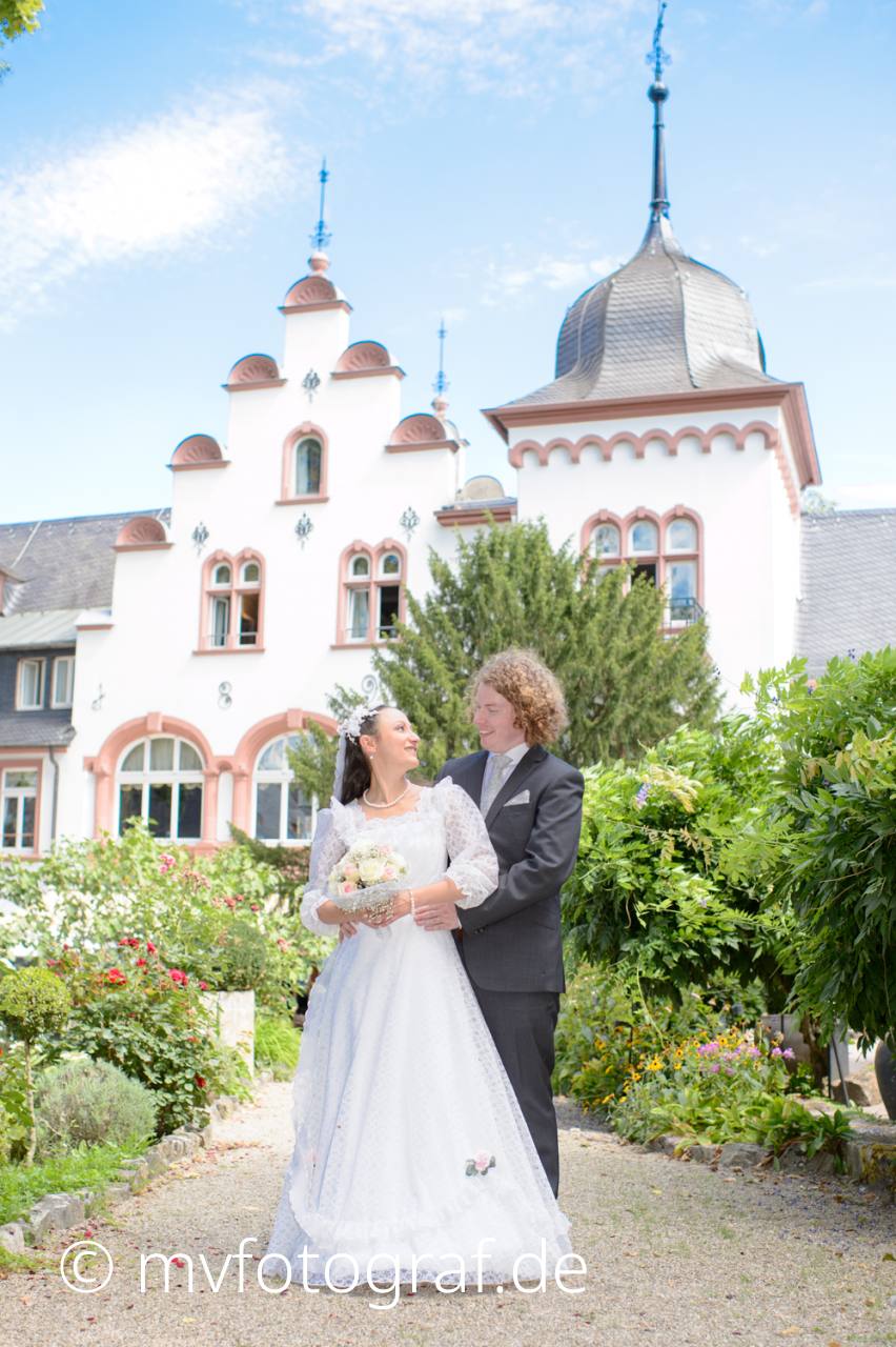 Brautpaar im Garten Ein Brautpaar steht nebeneinander in einem Garten. Im Hintergrund ist das Kronenschlösschen zu sehen.