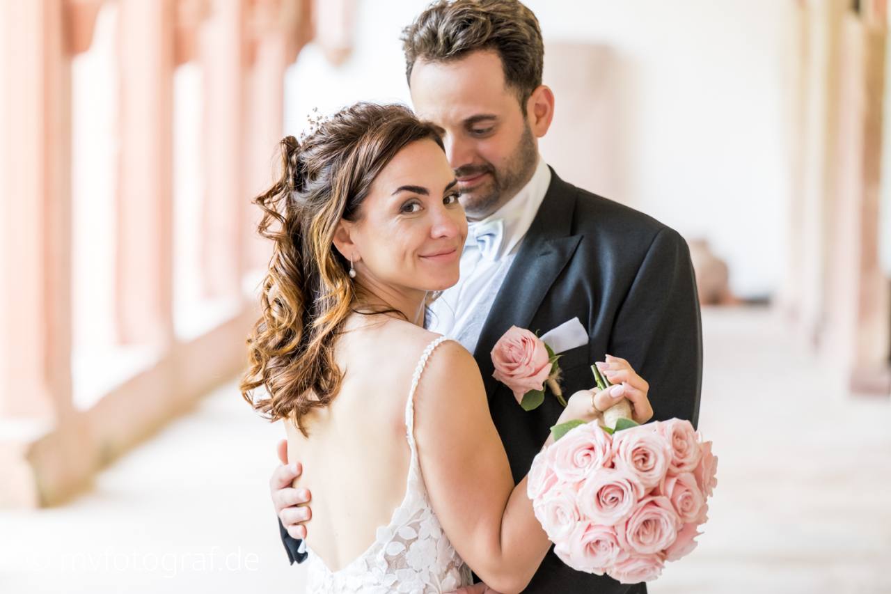 Brautpaar Umarmung Ein Hochzeitspaar steht sich gegenüber. Die Frau guckt über die Schulter und hält ihren Brautstrauß lässig in der Hand.