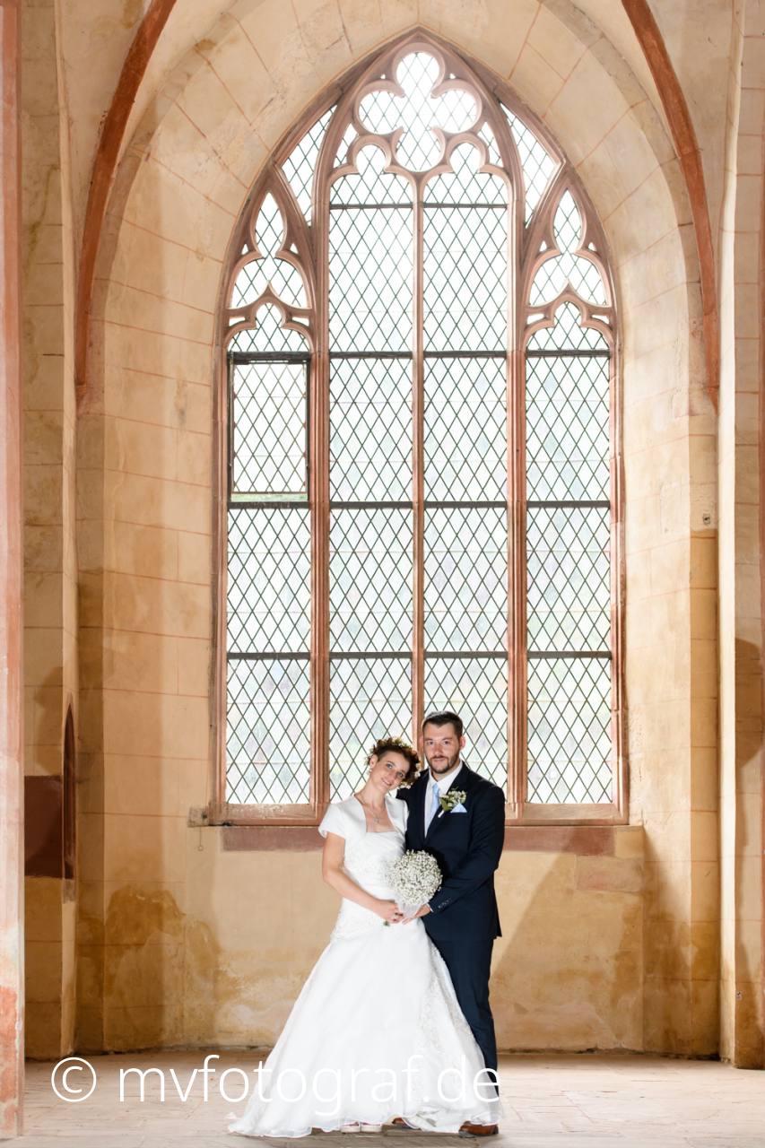 Umarmung vor Kirchenfenster Ein paar steht in einer Kirche. Im Hintergrund ein großes Gothisches Fenster.