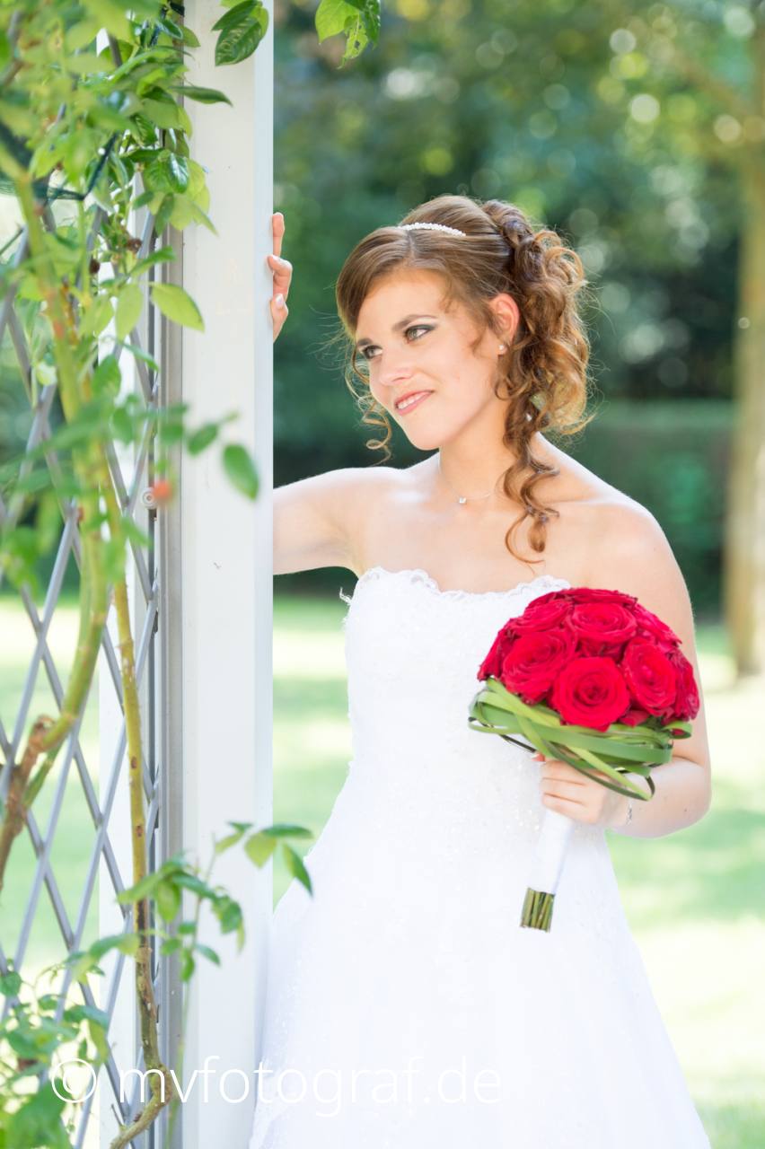 Braut an Rankgitter Eine Braut im weissen Hochzeitskleid steht an einem Rankgitter mit Ihrem Brautstrauss in der Hand