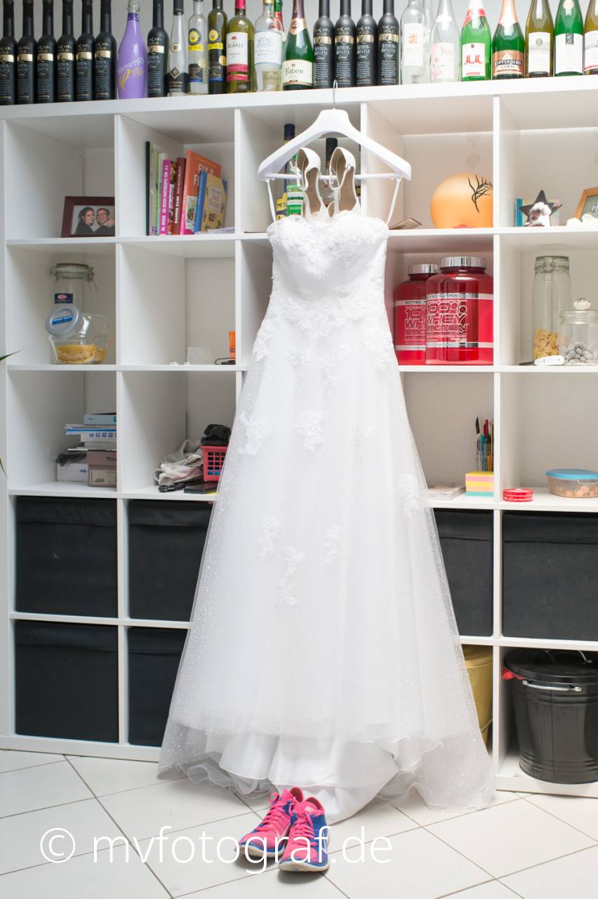 Brautkleid und Turnschuhe Ein Brautkleid hängt an einer Regalwand. Davor stehen Turnschuhe.