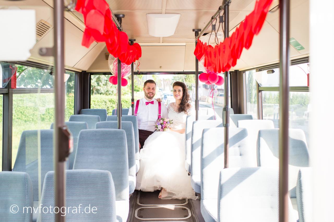 Ein Brautpaar sitzt auf der letzten Bank in einem Bus. Die Haltestangen sind but geschmückt.